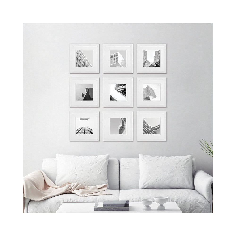 Nine white framed black and white architectural photographs arranged in a 3x3 grid on a light gray wall above a white sofa with pillows.