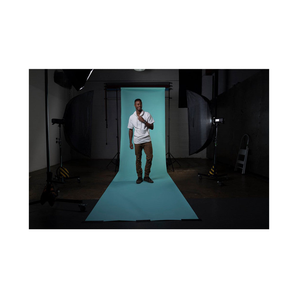 Professional studio setup showing turquoise seamless background paper in use with male subject, professional lighting, and equipment visible.